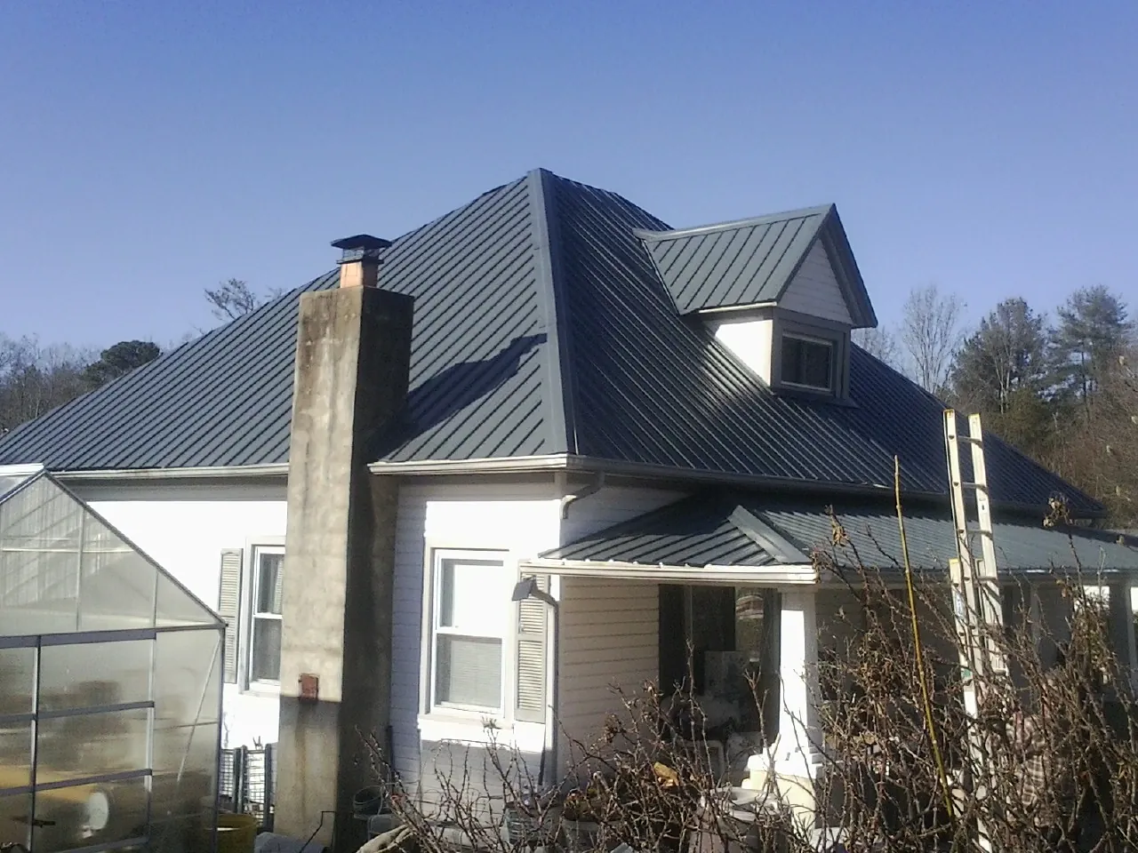 Dark blue standing seam metal roof on a white farmhouse with dormer — Slate & Tile Roof Repair by Roofing Brothers in Knippa