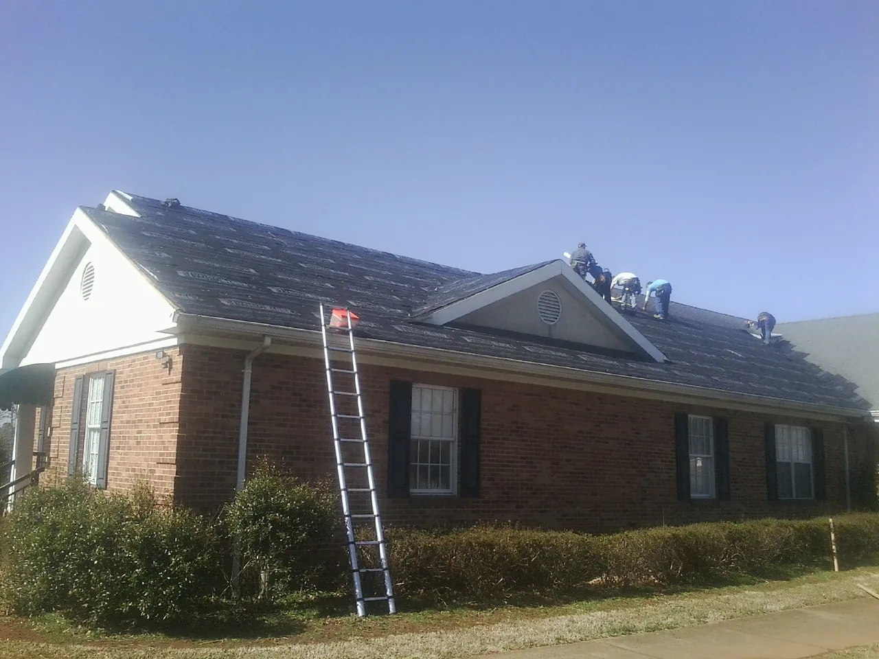 Crew tearing shingles off a brick ranch roof with a ladder set — Metal Roof Repair work by our crew in Knippa