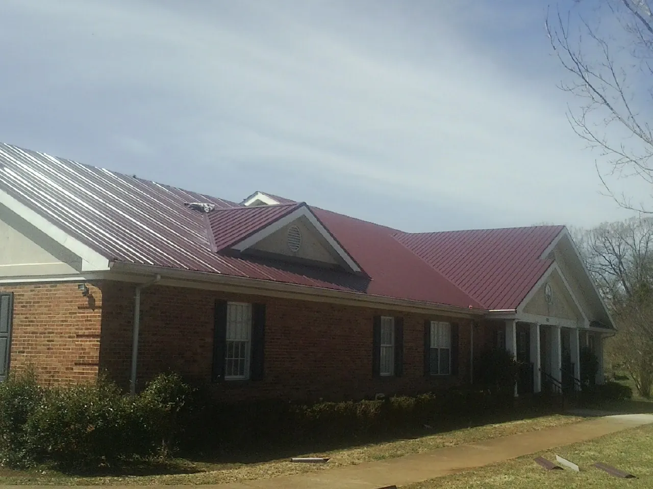 Red metal roof with gabled entries on a long brick building, from a Hail Damage Roof Repair job in Knippa