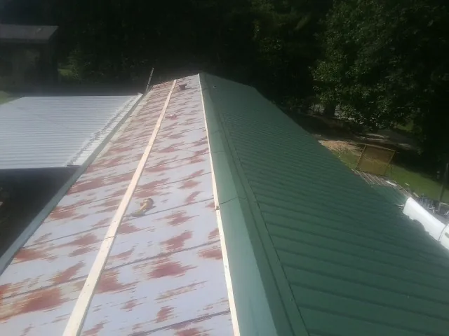 Old rusted panels beside newly installed green metal roofing — Wind Damage Roof Repair by Roofing Brothers in Knippa